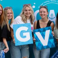 six students posing in front of CAB backdrop at Laker Kickoff photo booth and holding GV letters